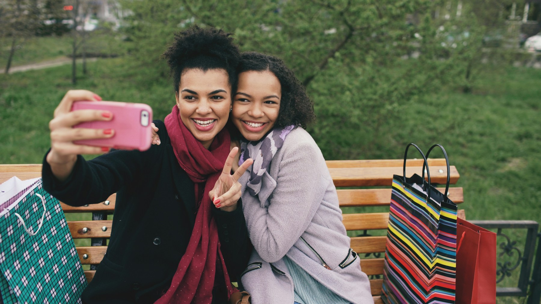 Two smiling women taking a selfie with shopping bags.